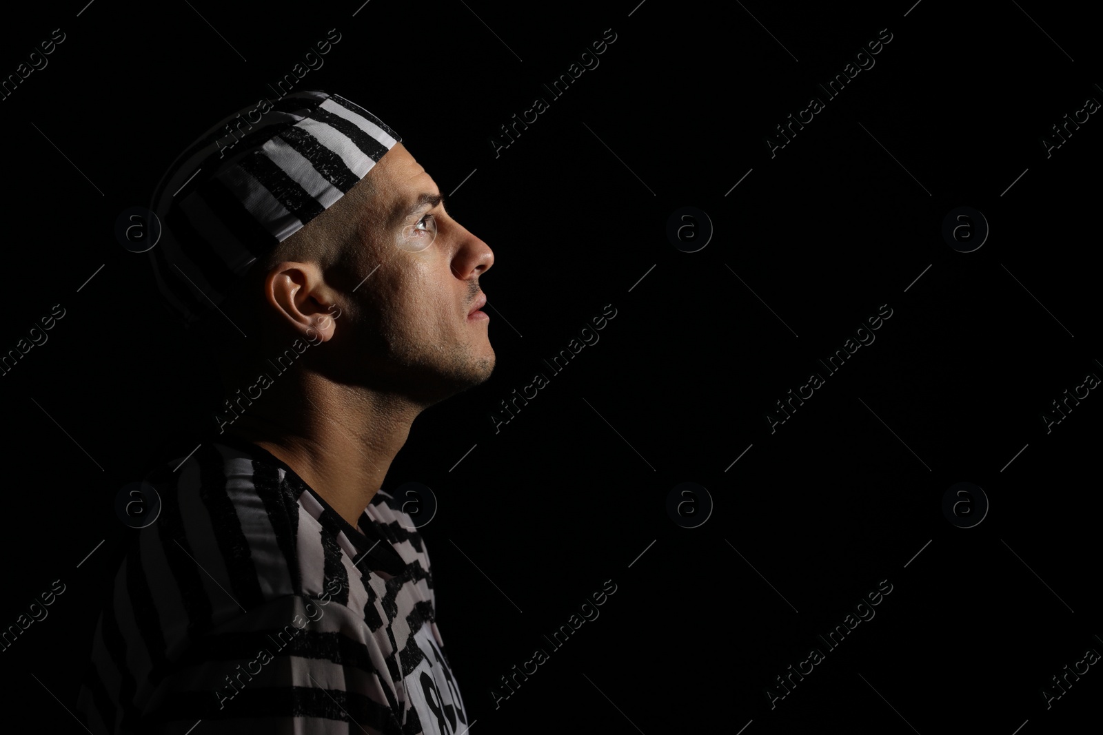 Photo of Remorseful prisoner in striped uniform on black background, space for text