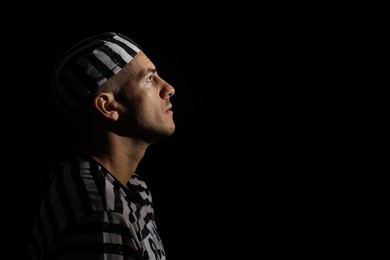 Photo of Remorseful prisoner in striped uniform on black background, space for text