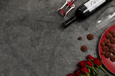Photo of Red wine, chocolate truffles, roses and corkscrew on gray table, flat lay. Space for text