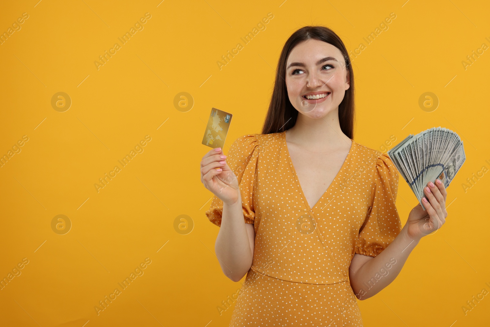 Photo of Happy woman with credit card and dollar banknotes on orange background, space for text