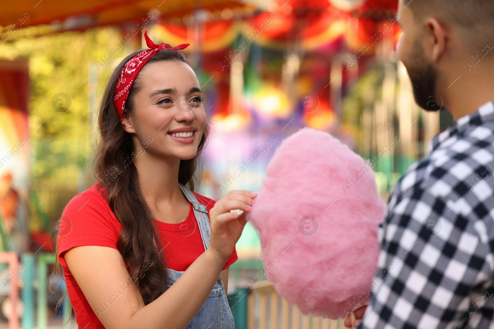 Photo of Happy young woman taking piece of cotton candy from his boyfriend at funfair