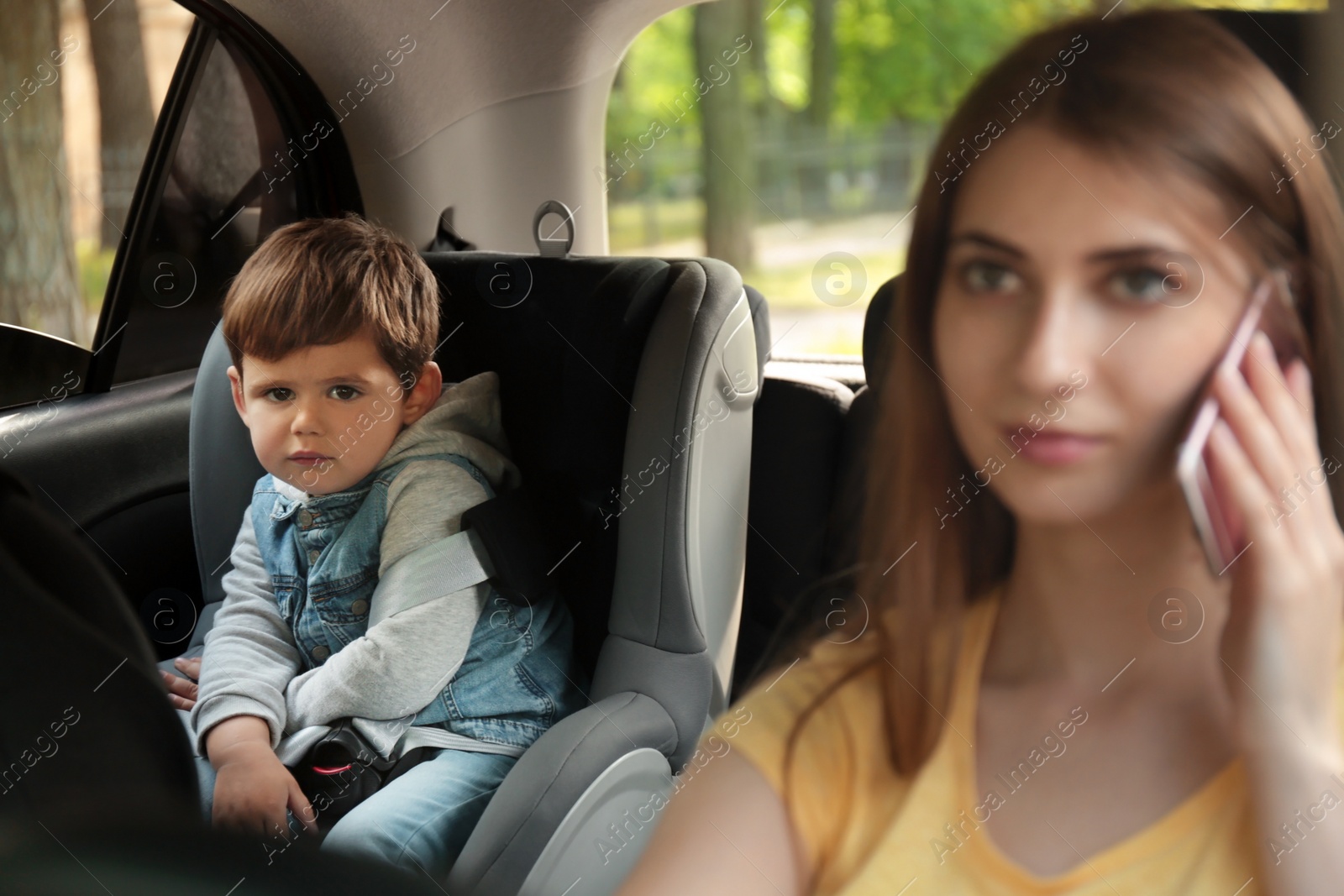 Photo of Mother talking by phone while driving car with her son on backseat. Child in danger