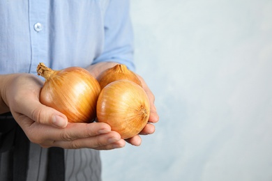 Photo of Woman holding handful of ripe onions on blue background, closeup with space for text