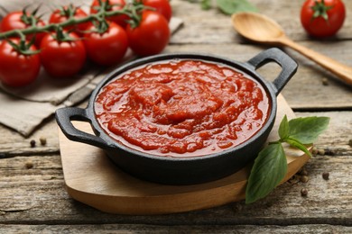 Homemade tomato sauce in bowl and basil on wooden table, closeup