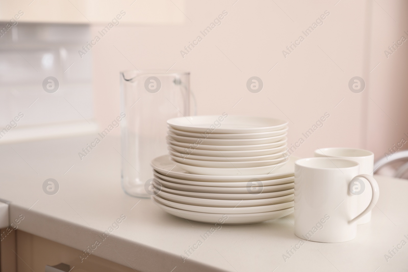 Photo of Stack of clean dishes, cups and glass jug on table in kitchen