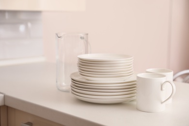 Photo of Stack of clean dishes, cups and glass jug on table in kitchen