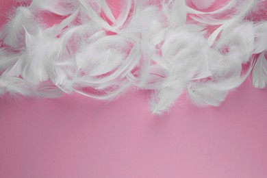 Photo of Many fluffy white feathers on pink background, flat lay. Space for text