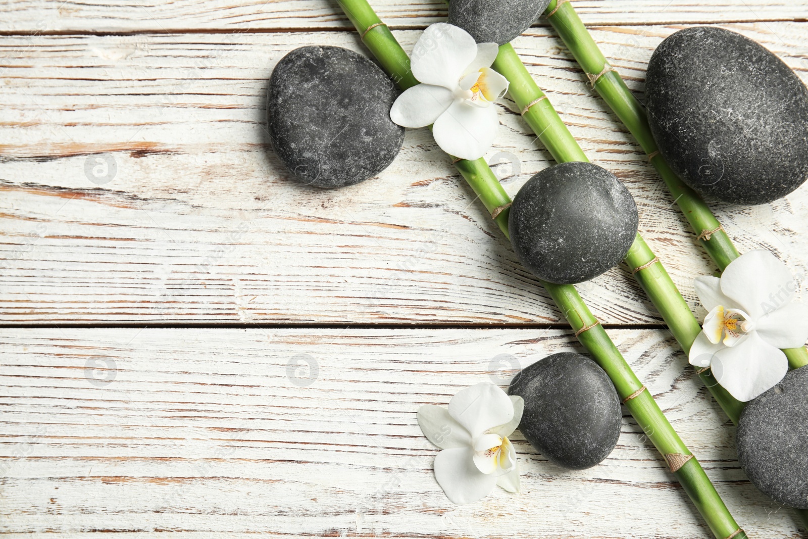 Photo of Flat lay composition with bamboo branches and spa stones on wooden background. Space for text