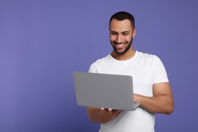 Photo of Smiling young man working with laptop on lilac background, space for text