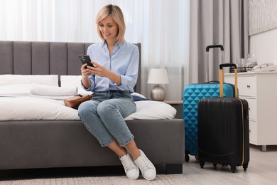 Photo of Smiling guest with smartphone on bed in stylish hotel room