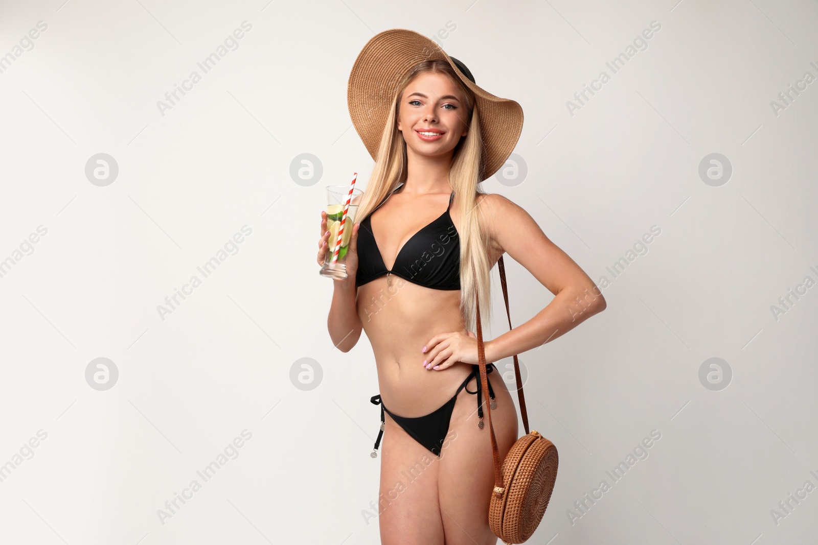 Photo of Pretty young woman wearing stylish bikini with purse and cocktail on light background