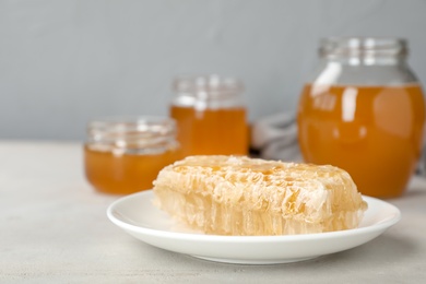 Photo of Plate with fresh honeycomb and jars on table