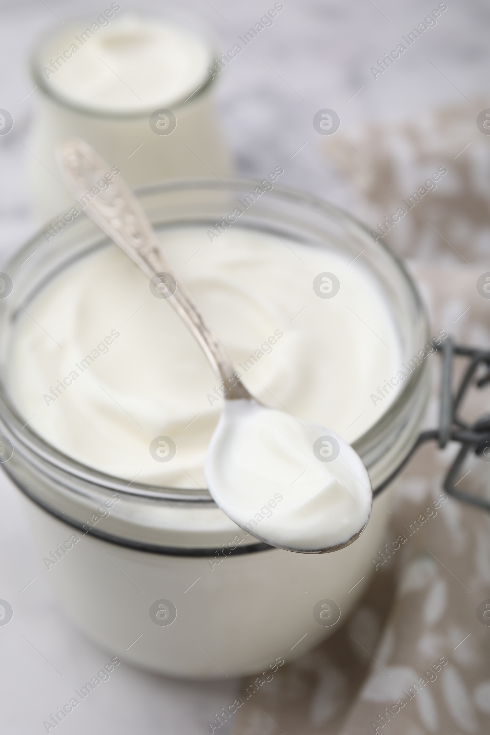 Photo of Delicious natural yogurt in glass jar and spoon on table, closeup