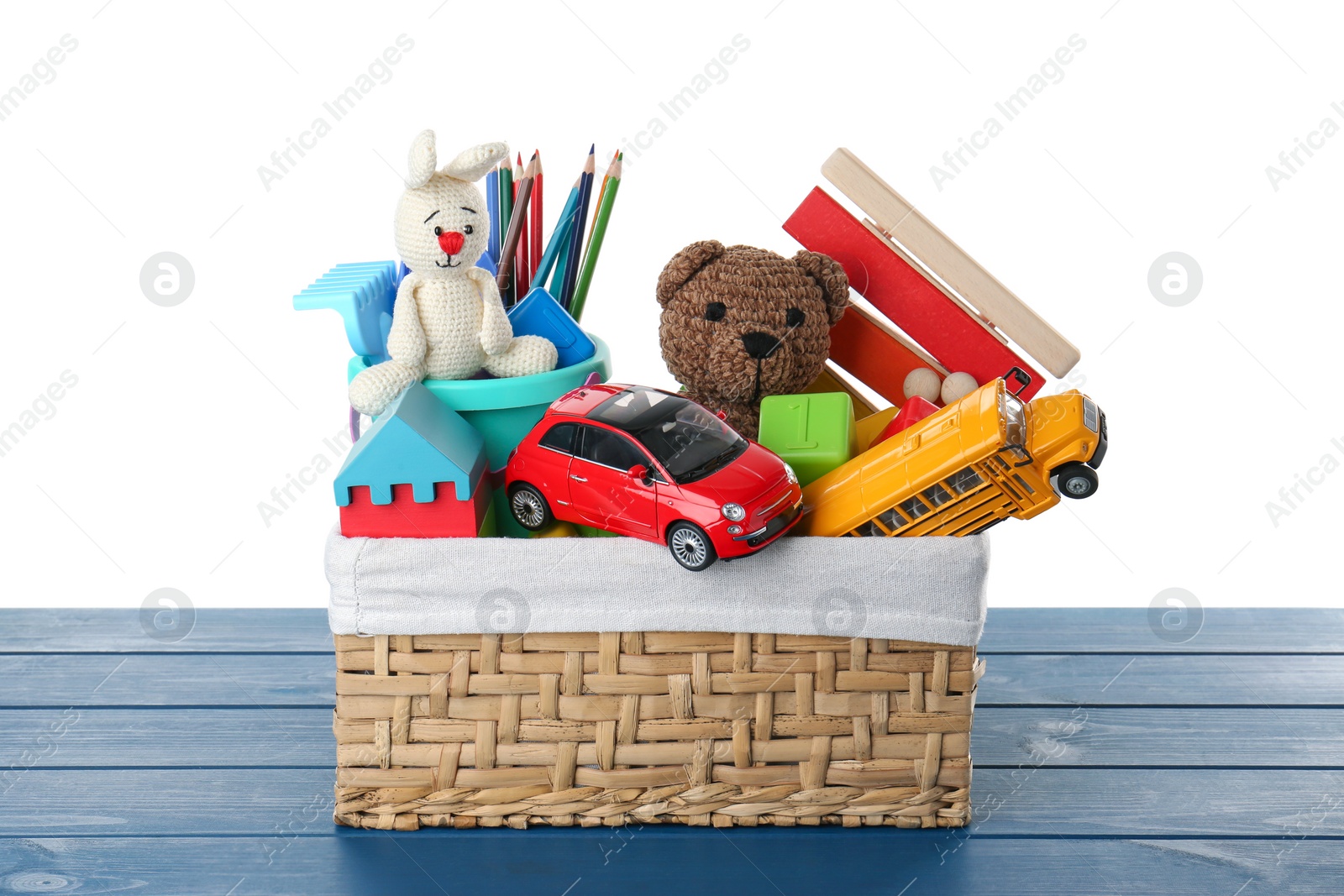 Photo of Wicker basket with different children's toys on blue wooden table against white background