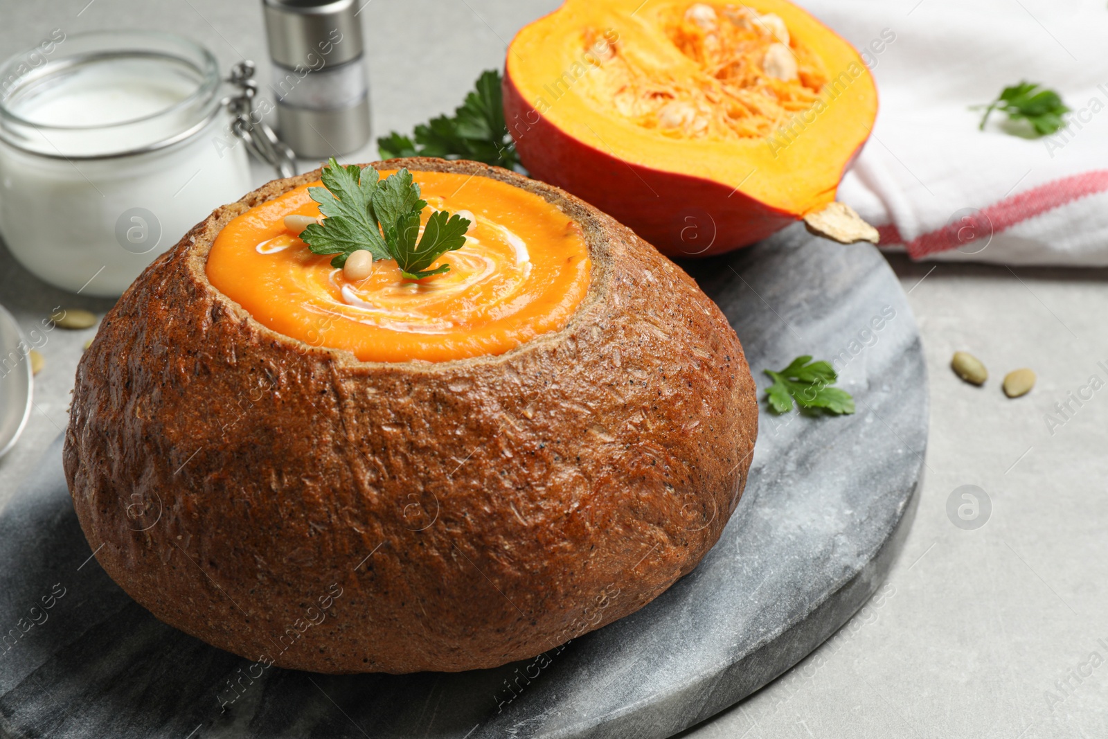 Photo of Tasty pumpkin cream soup in bread loaf on grey table