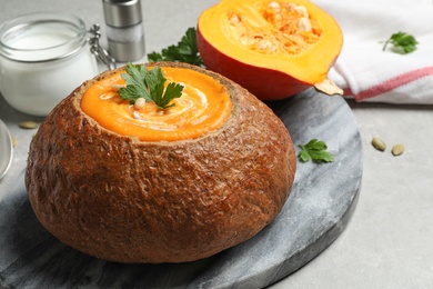 Photo of Tasty pumpkin cream soup in bread loaf on grey table