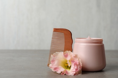 Photo of Hair product, flower and wooden comb on grey table. Space for text