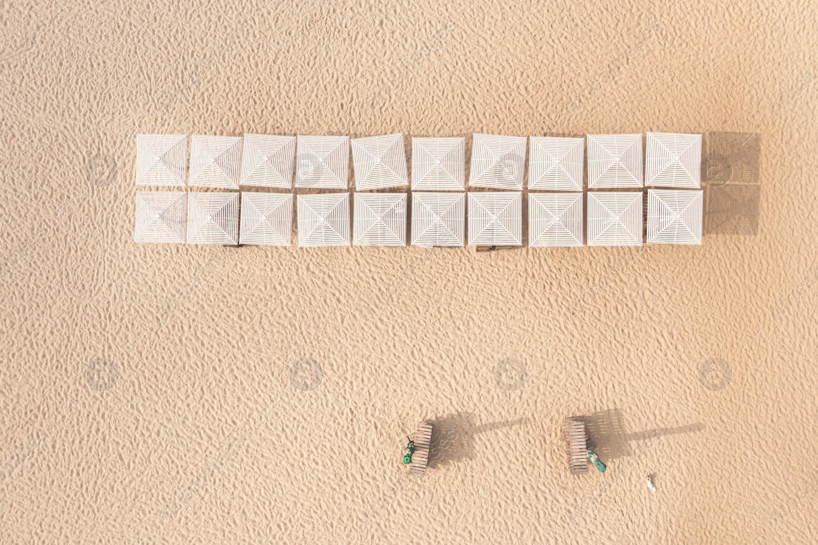 Image of Many beach umbrellas and wooden sunbeds on sandy coast, aerial view