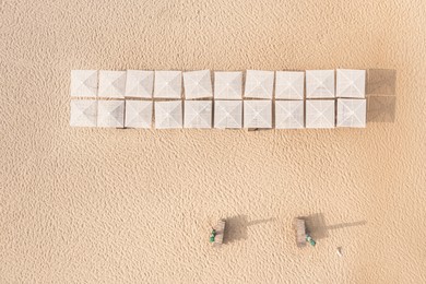 Image of Many beach umbrellas and wooden sunbeds on sandy coast, aerial view