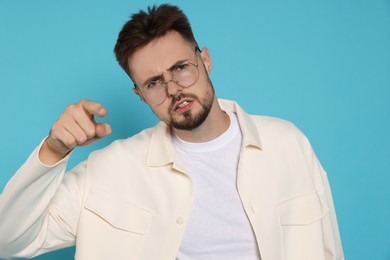 Aggressive man in white jacket and eyeglasses pointing finger on light blue background