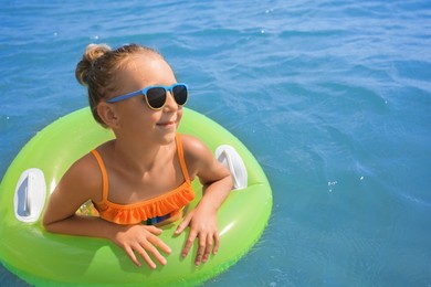 Photo of Little girl with sunglasses and inflatable ring in sea on sunny day. Beach holiday