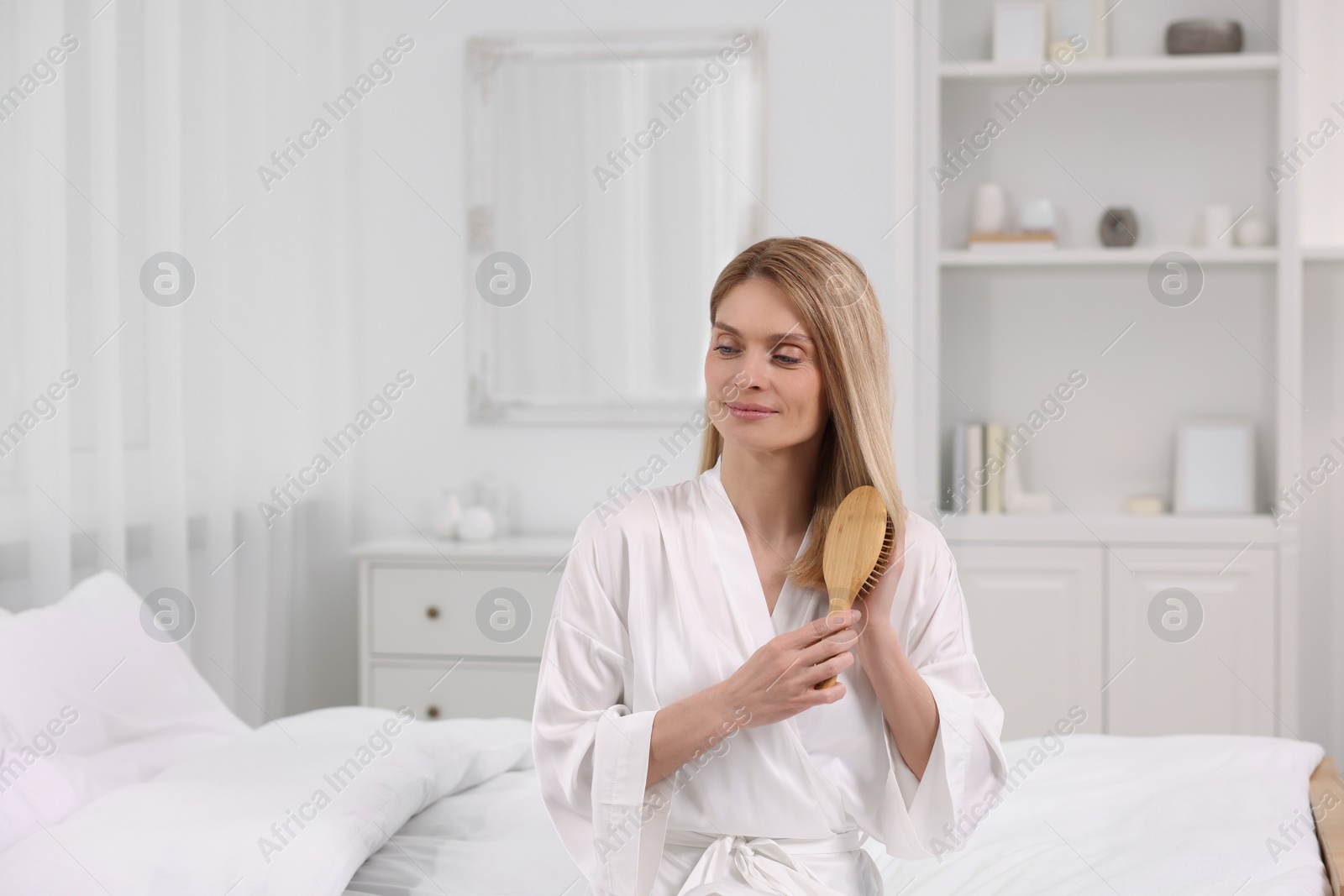 Photo of Beautiful woman brushing her hair on bed in room