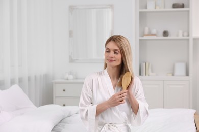 Beautiful woman brushing her hair on bed in room