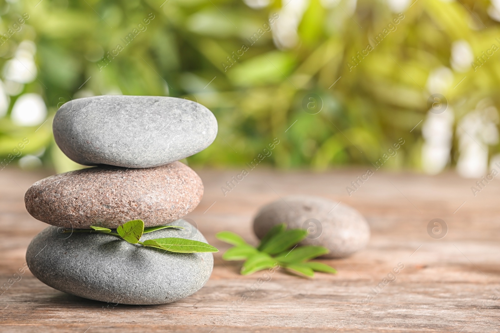 Photo of Spa stones and bamboo leaves on table against blurred background. Space for text