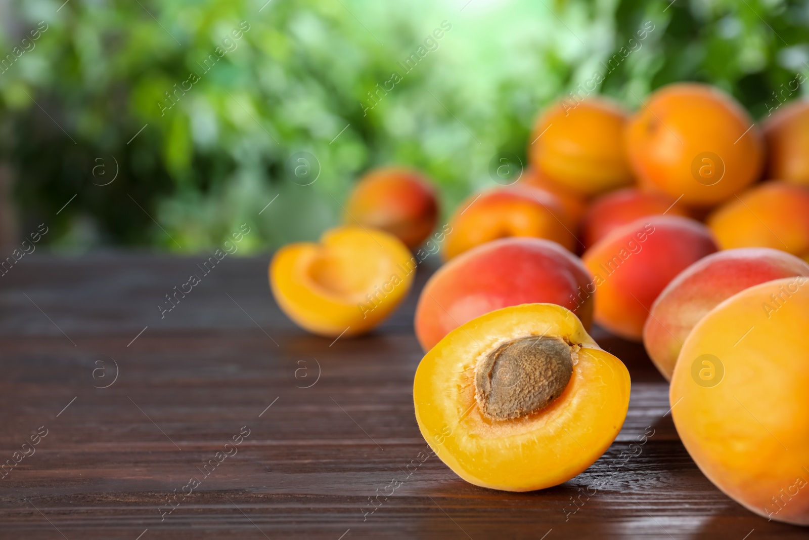 Photo of Many fresh ripe apricots on wooden table against blurred background. Space for text