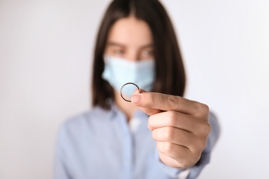 Woman in protective mask holding wedding ring against light background, focus on hand. Divorce during coronavirus quarantine