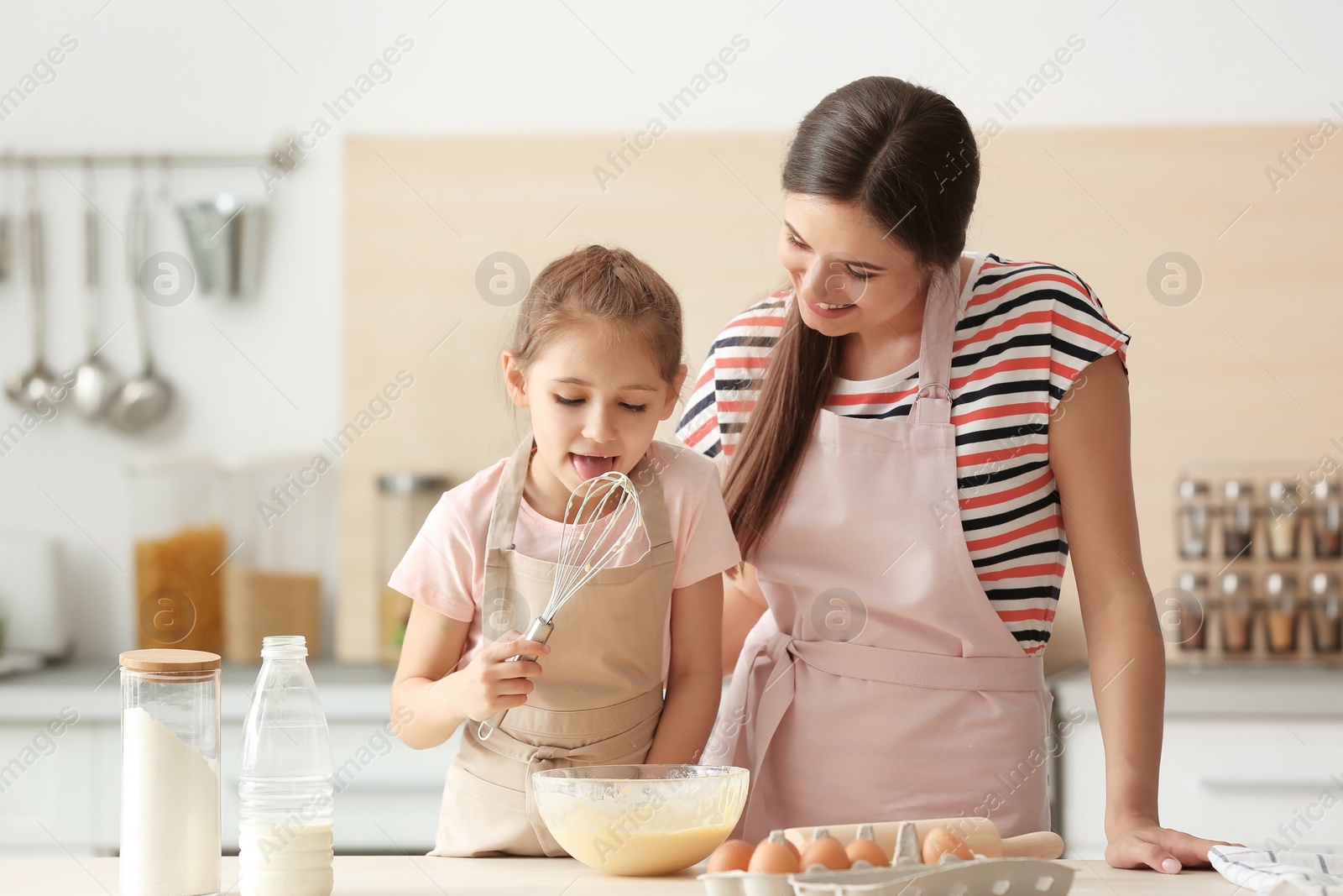 Photo of Mother and her daughter making dough at table in kitchen