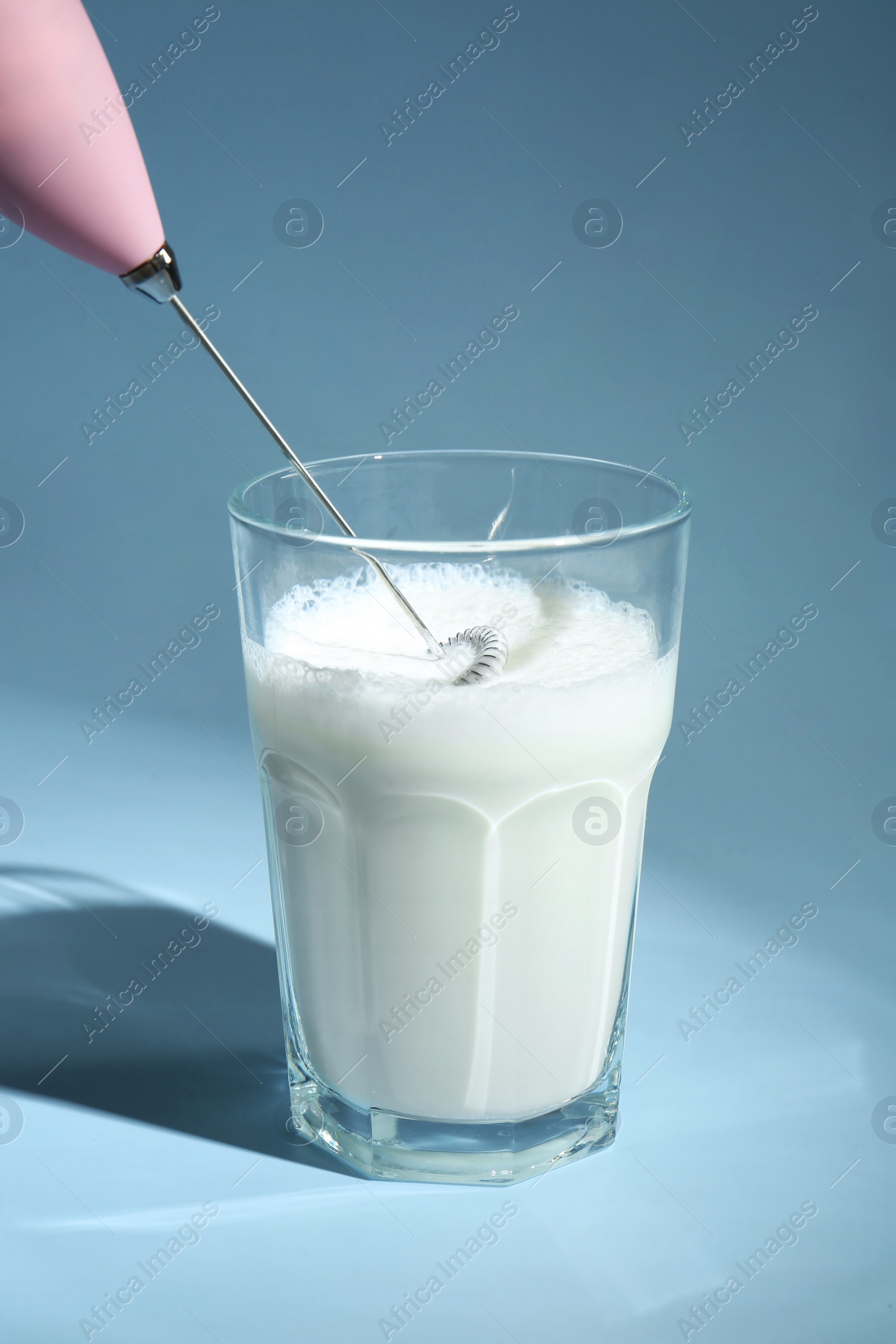 Photo of Whisking milk in glass with mini mixer (milk frother) on light blue background