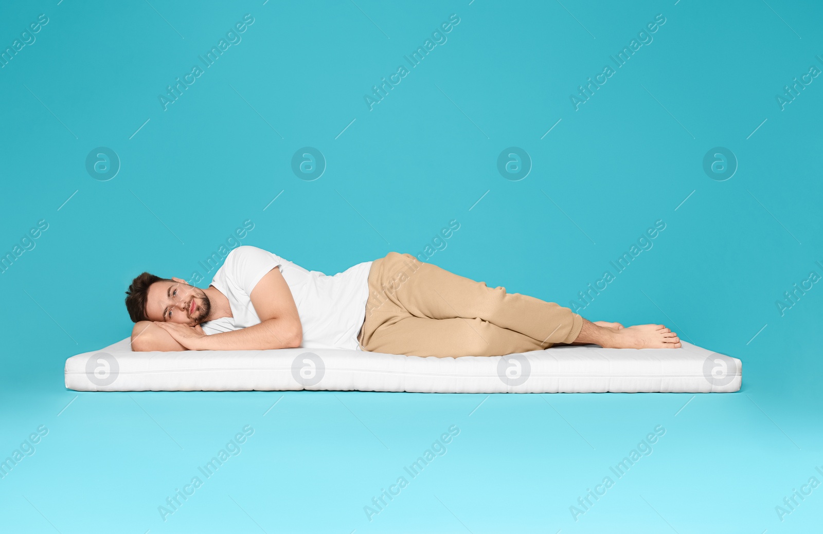 Photo of Man lying on soft mattress against light blue background