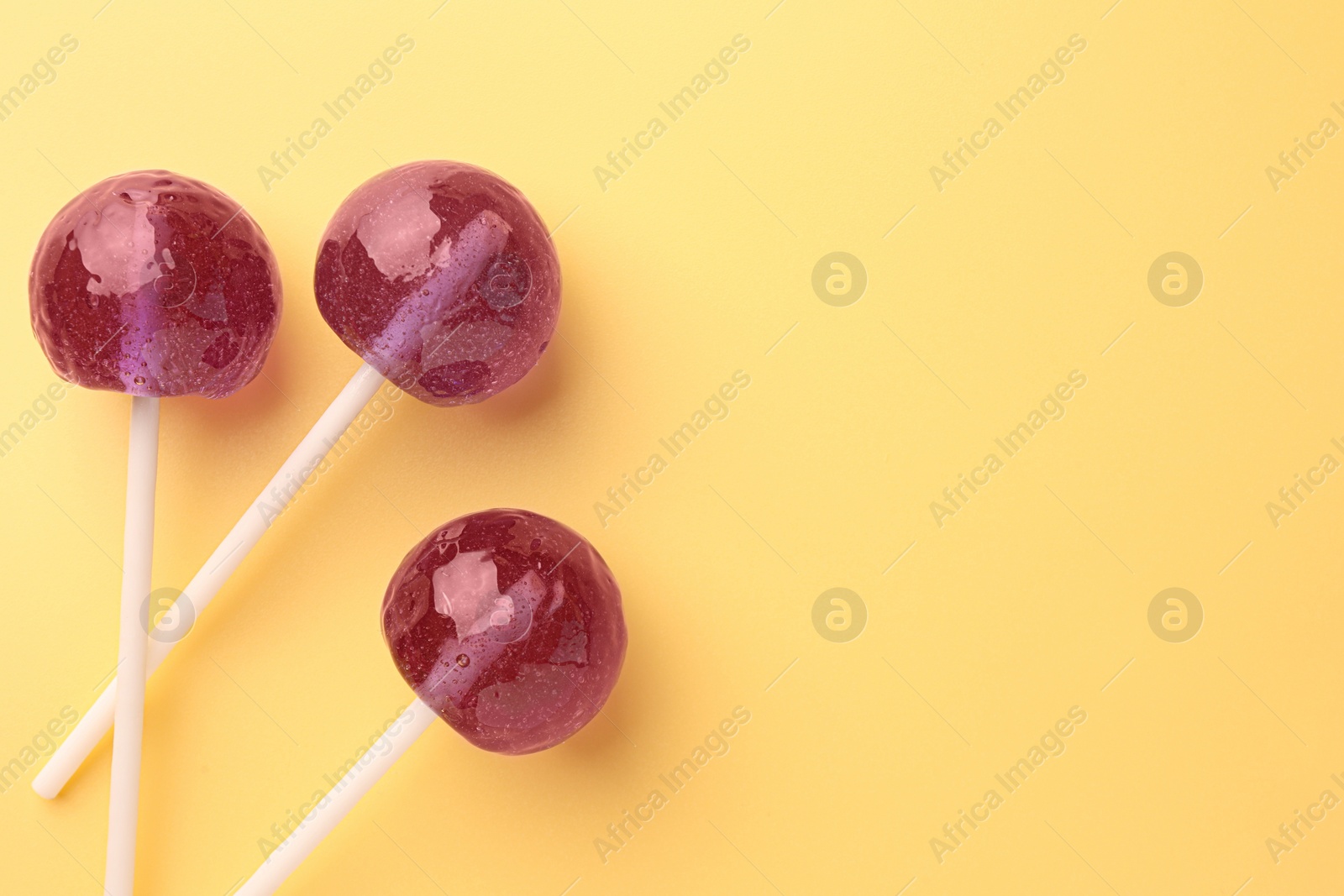 Photo of Tasty lollipops on yellow background, flat lay. Space for text