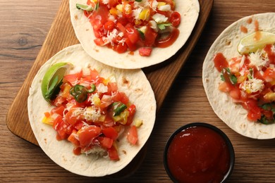 Delicious tacos with vegetables, lime and ketchup on wooden table, flat lay