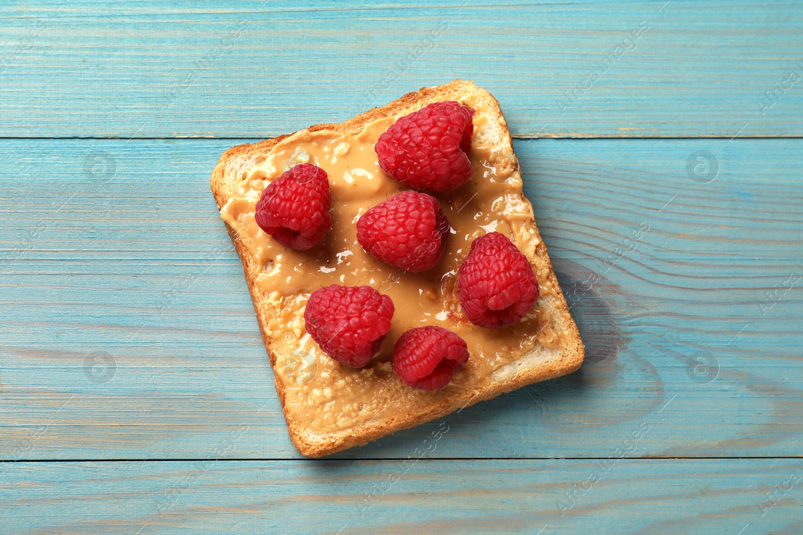 Photo of Delicious toast with peanut butter and raspberries on light blue wooden table, top view