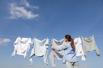 Woman hanging clothes with clothespins on washing line for drying against cloudy sky outdoors
