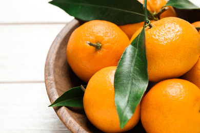 Fresh ripe tangerines with leaves in wooden bowl on white table, closeup. Citrus fruit