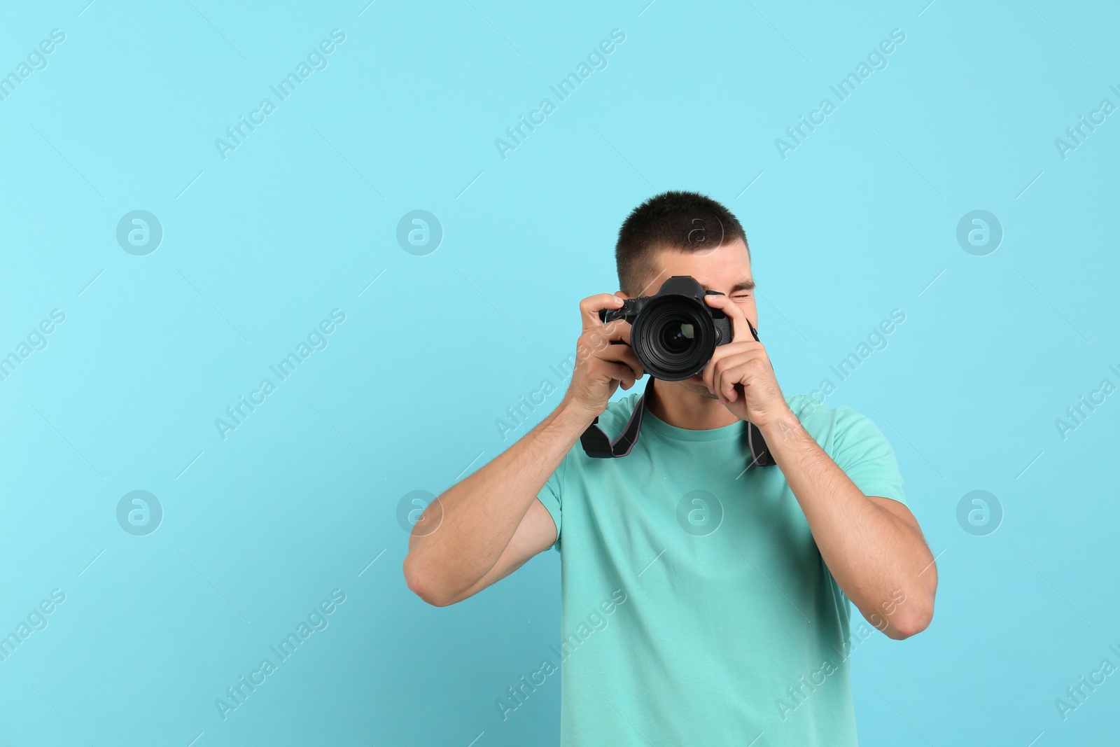 Photo of Young professional photographer taking picture on light blue background. Space for text