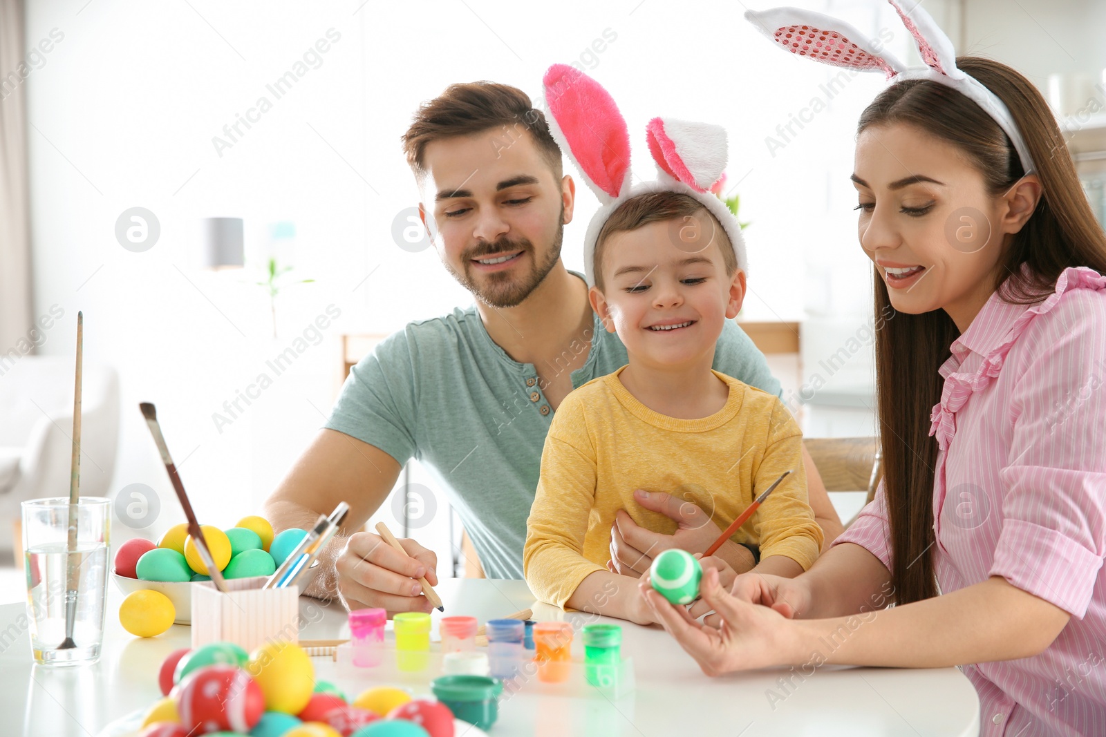 Photo of Happy family painting Easter eggs in kitchen. Festive tradition