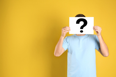 Photo of Man holding paper with question mark on yellow background, space for text