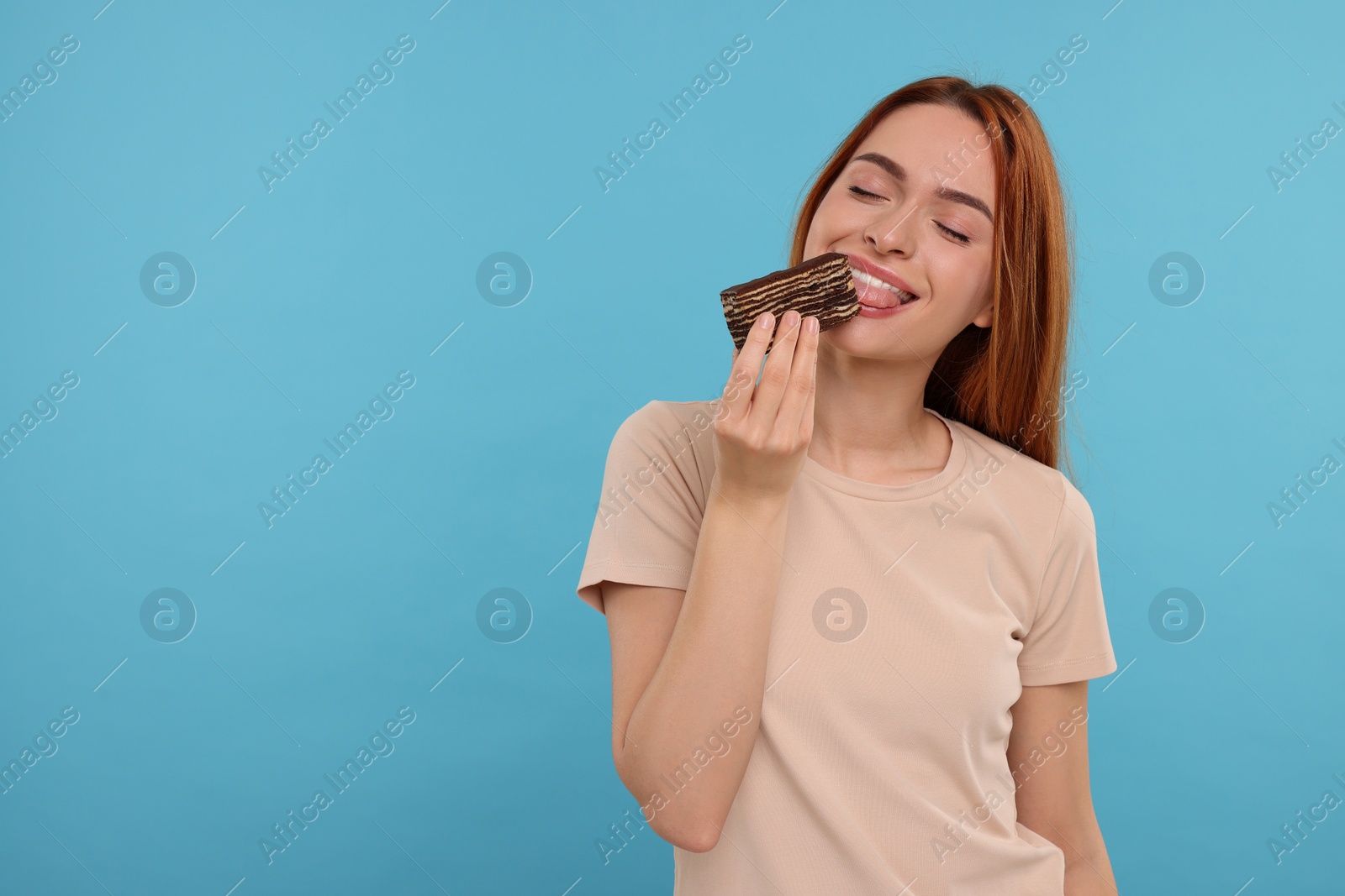 Photo of Young woman eating tasty cake on light blue background, space for text