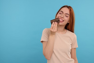 Young woman eating tasty cake on light blue background, space for text