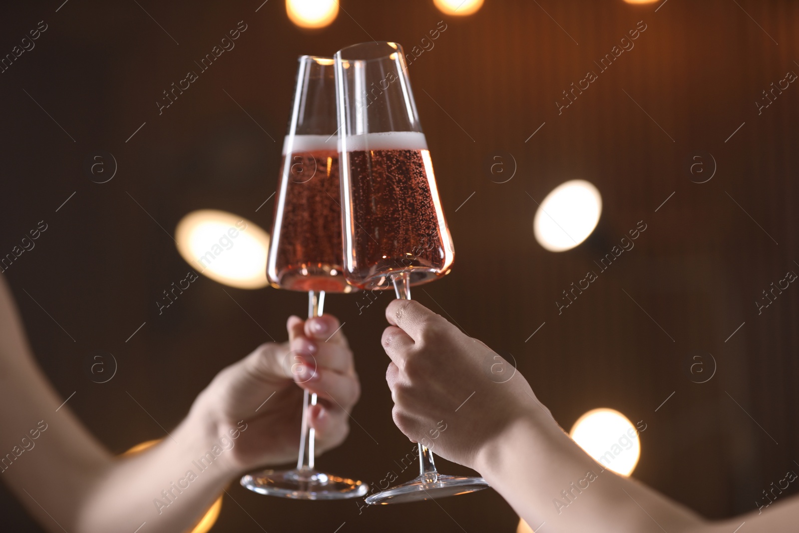 Photo of Women clinking glasses with champagne against blurred lights, closeup