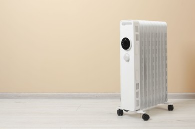 Modern portable electric heater on floor near beige wall indoors, space for text