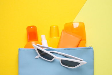 Sun protection products in bag and sunglasses on yellow background, top view