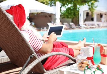 Authentic Santa Claus using tablet near pool at resort