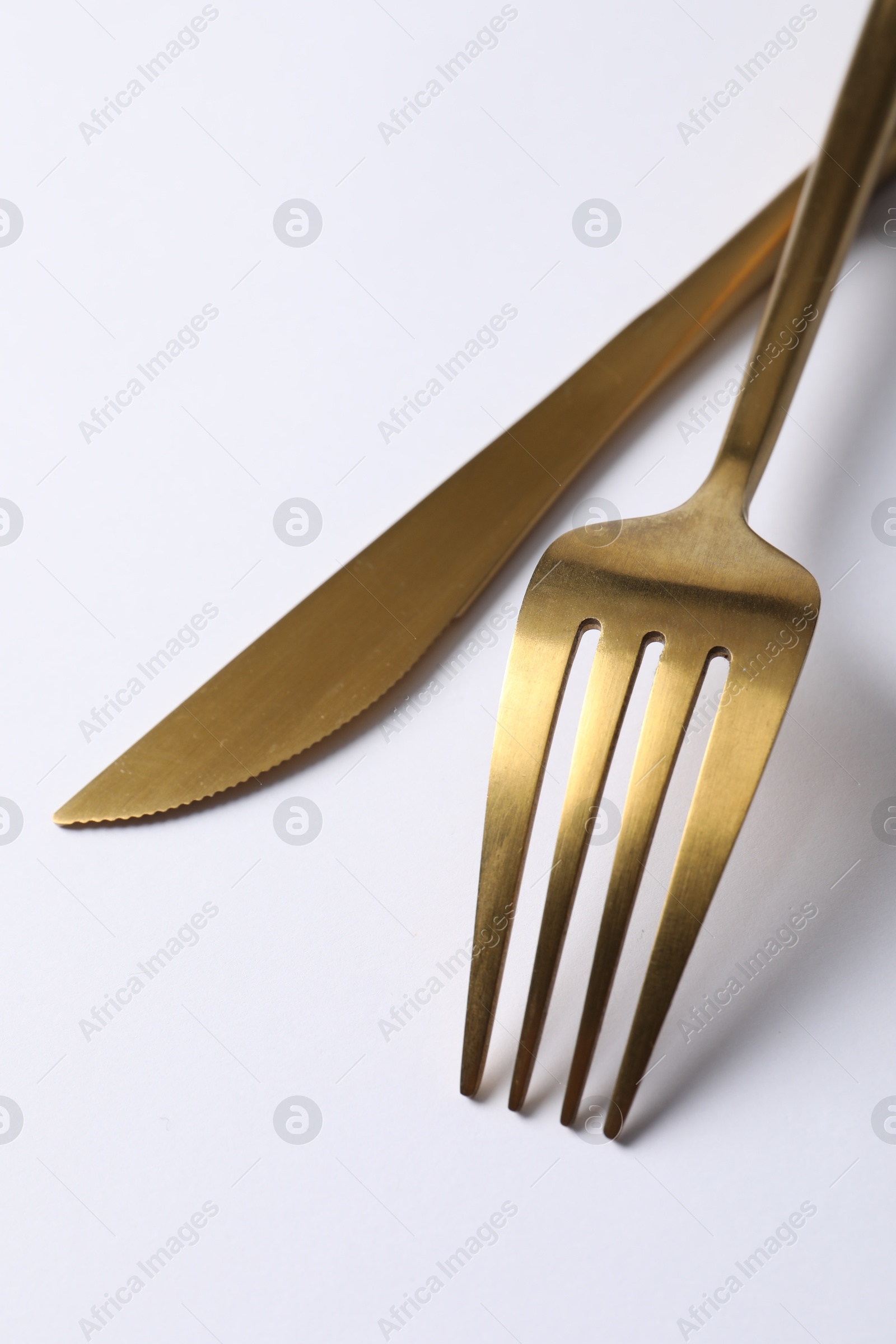 Photo of Stylish golden cutlery. Fork and knife on white background, closeup