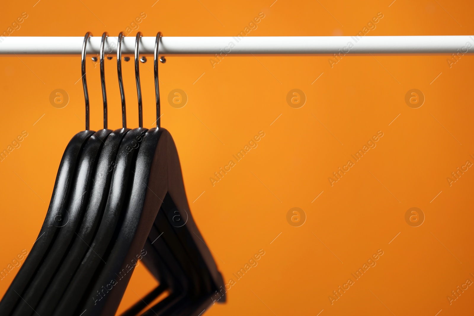 Photo of Black clothes hangers on rack against orange background, closeup. Space for text