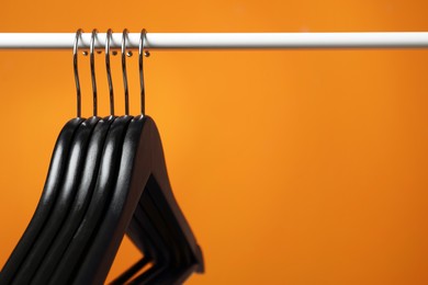 Photo of Black clothes hangers on rack against orange background, closeup. Space for text